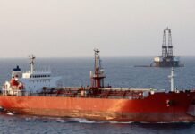 Oil tanker with low cargo, distant oil rigs, hazy sky.